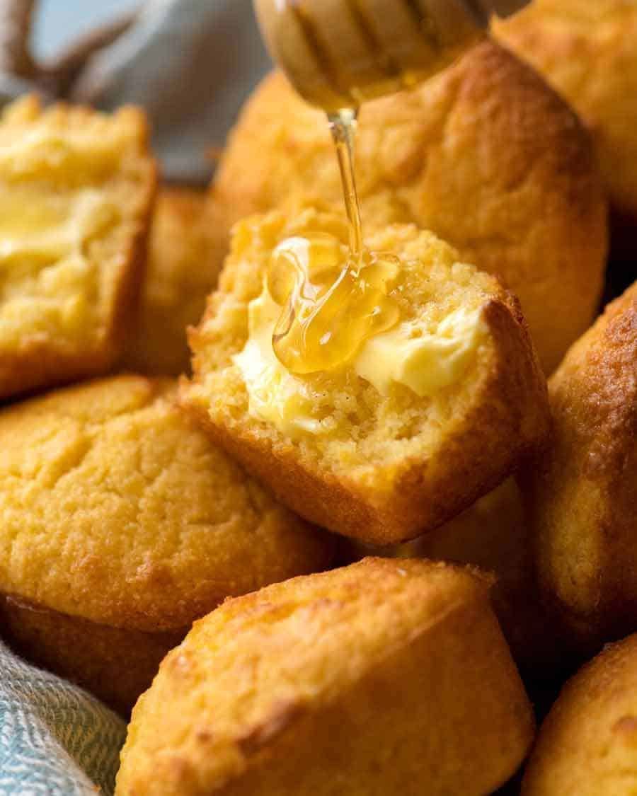 Cornbread Muffin broken in half slathered with butter and being drizzled with honey