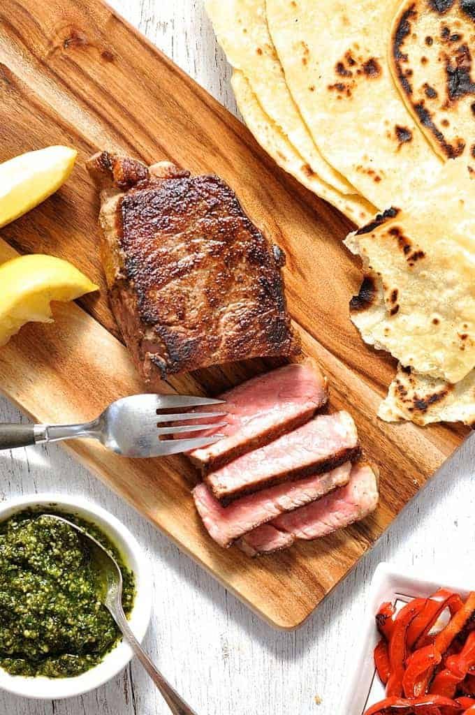 Steak with Pesto and chargrilled capsicum on a wooden board, ready to be eaten.