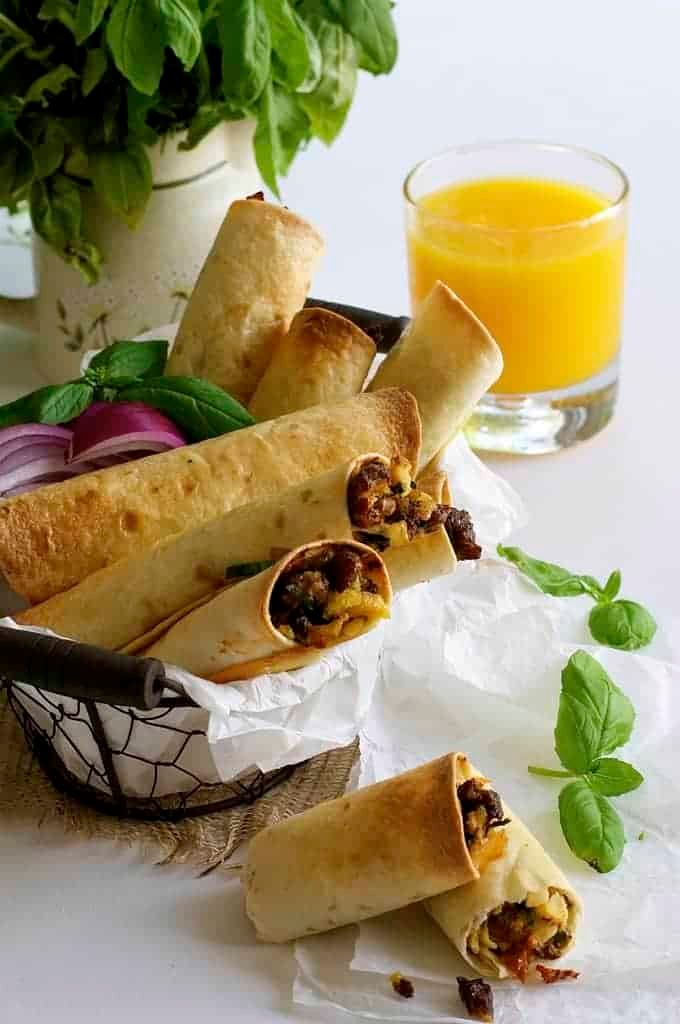 Spicy Italian Breakfast Roll Ups in a basket with glass of orange juice