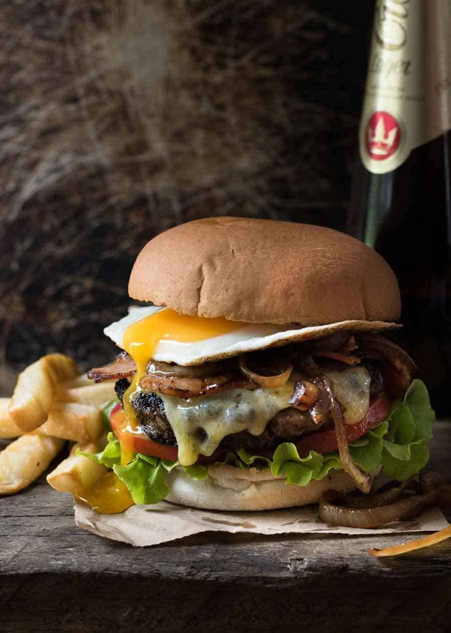Fully loaded Hamburger with bacon and egg, with a side of chips and beer, ready to be eaten