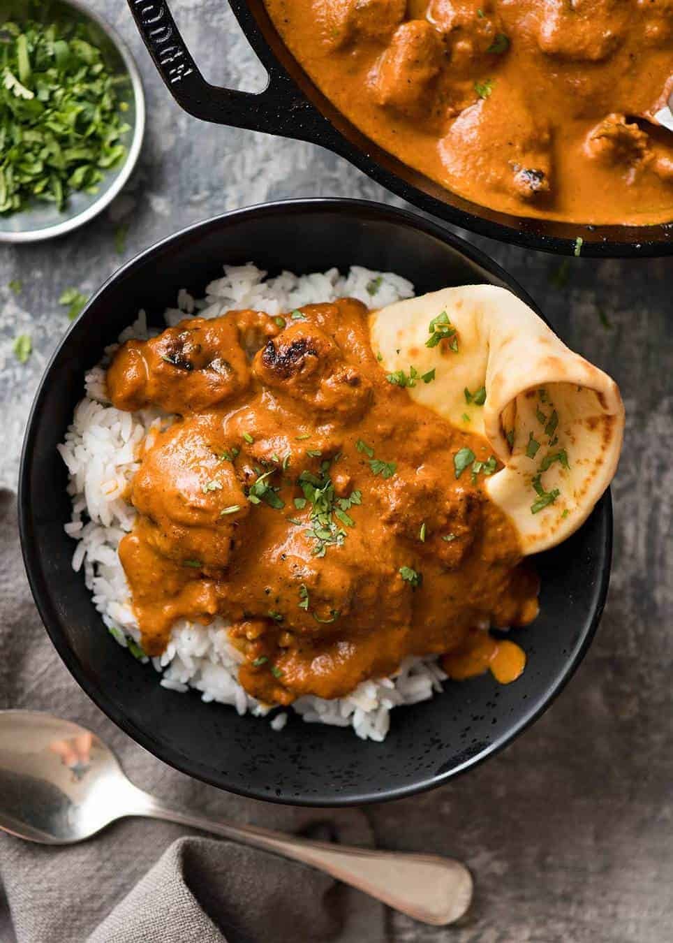 Overhead photo of chicken tikka masala on basmati rice in a dark rustic bowl with a piece of naan wedged in on the side.