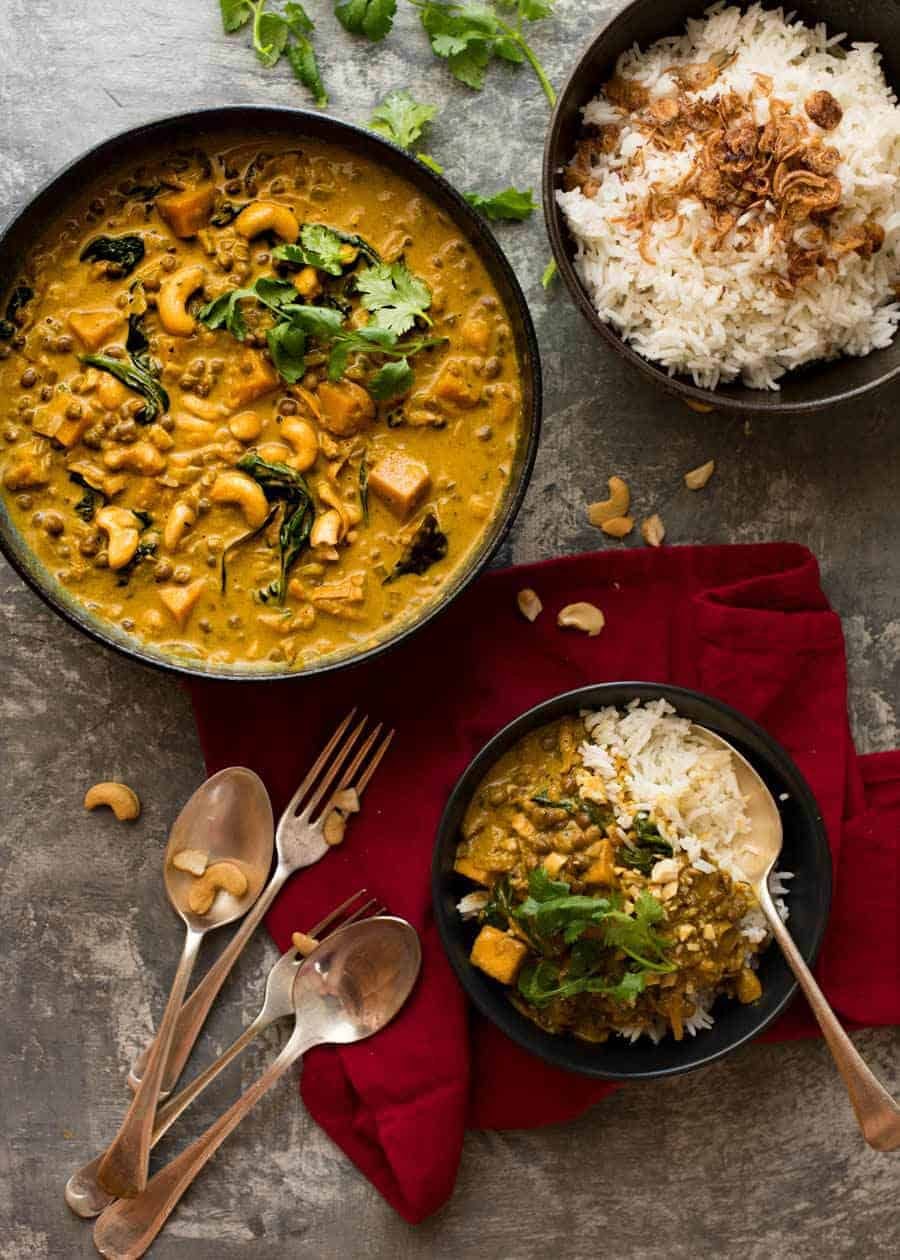 Tablescape overhead photo of Coconut Curry with Lentils & Pumpkin in a dark bowl with a side of rice, ready to be served.
