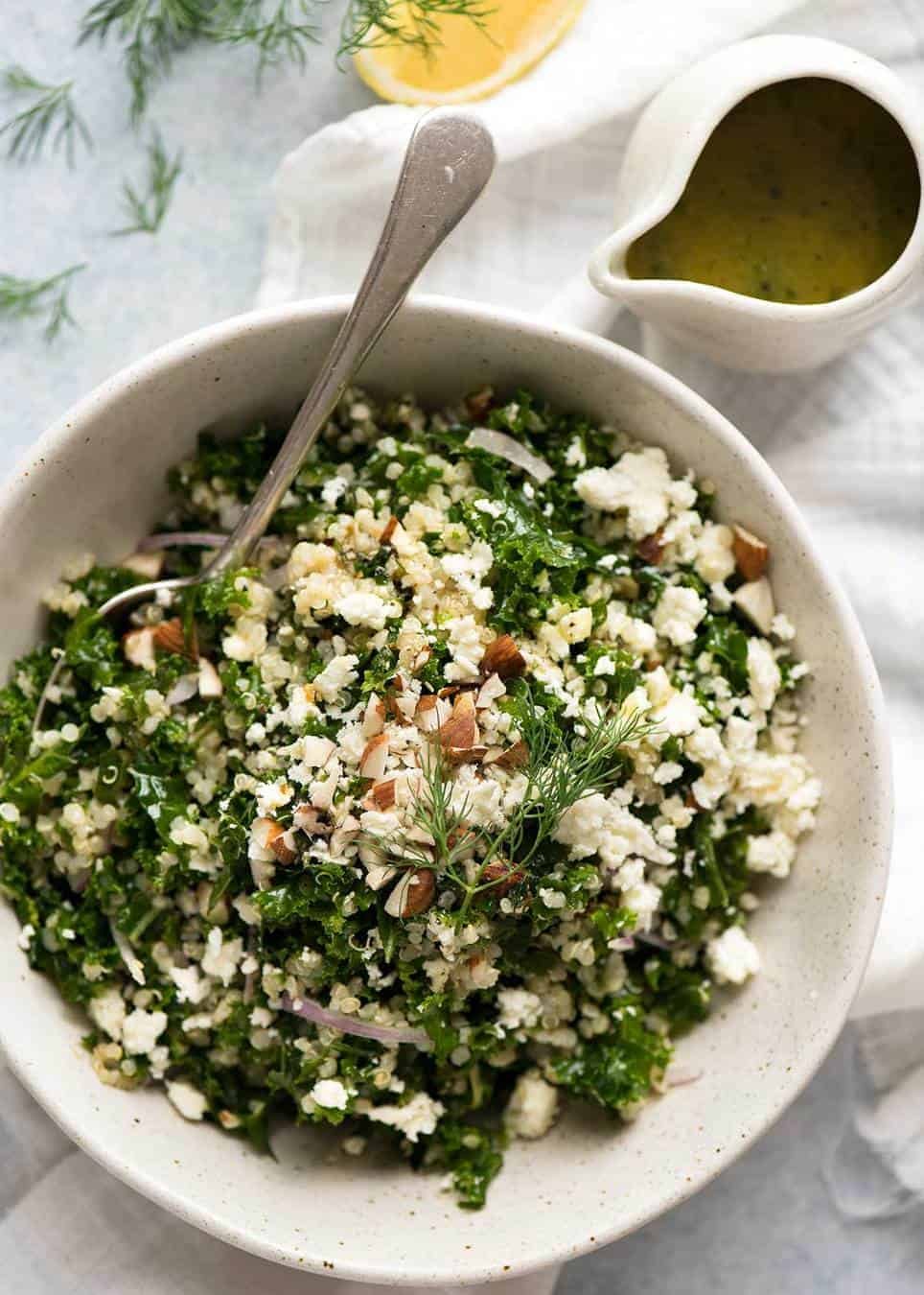 Overhead photo of Kale and Quinoa Salad in a white rustic salad bowl with a small jug of lemon dressing on the side.