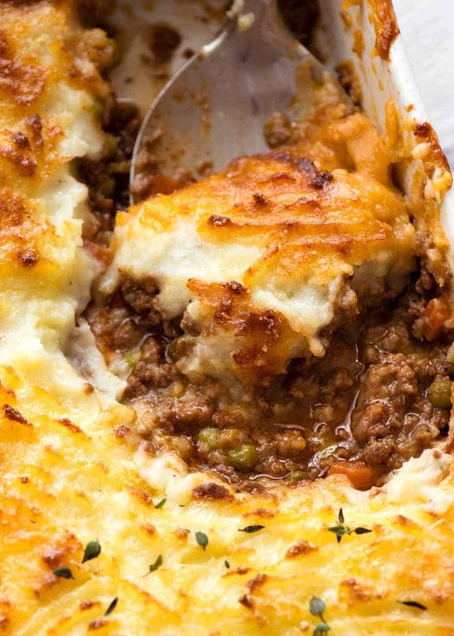 Close up of spoon scooping Shepherd's Pie out of a white baking dish, fresh out of the oven