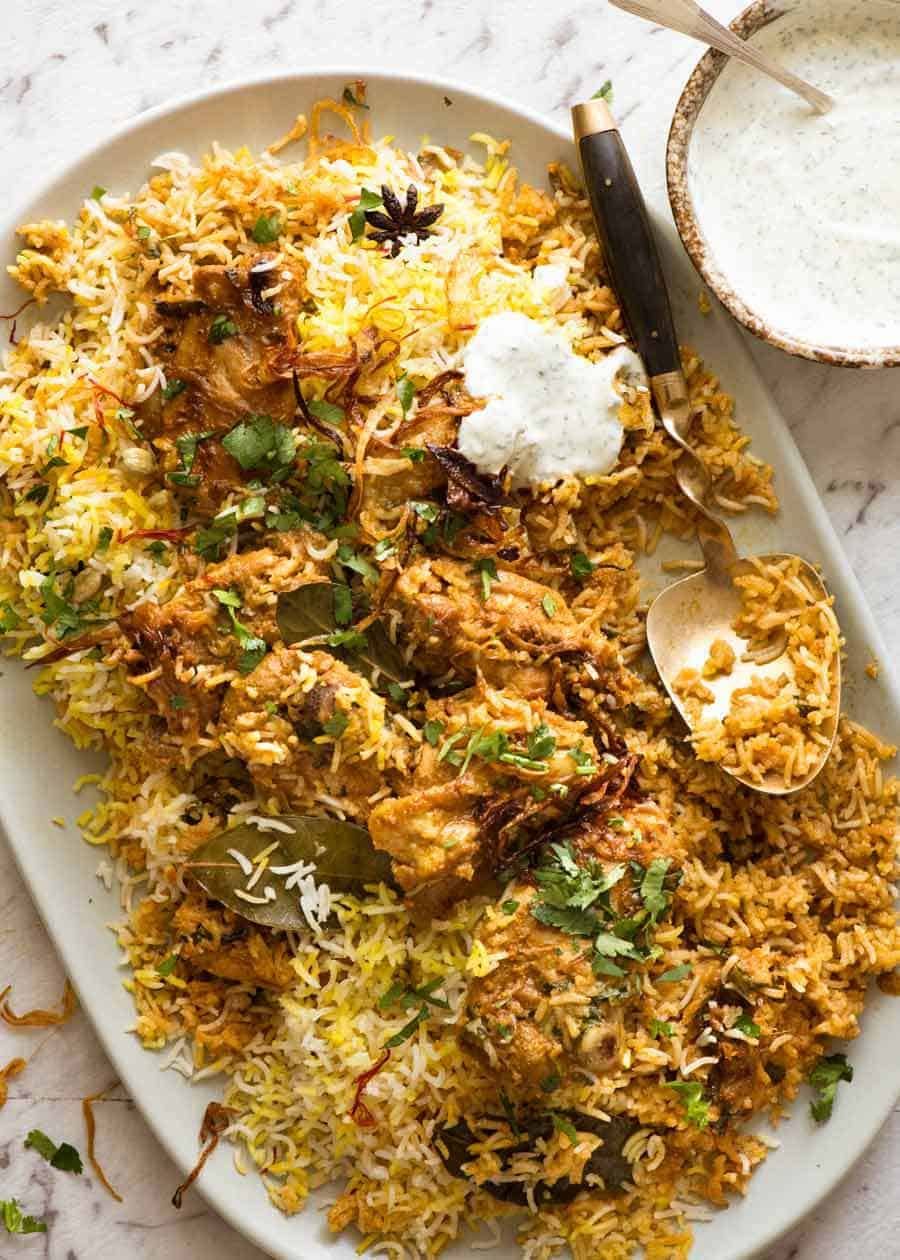 Chicken Biryani on a large serving platter, garnished with coriander with a side of minted yoghurt.