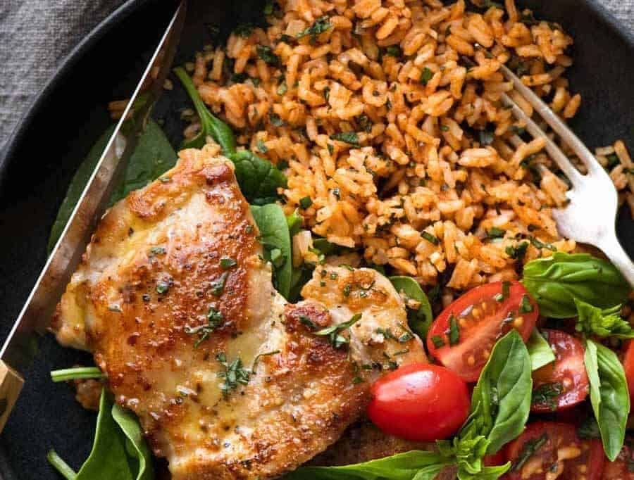 Crispy Garlic Chicken Thighs with Tomato Basil Rice in a black dish, ready to be eaten
