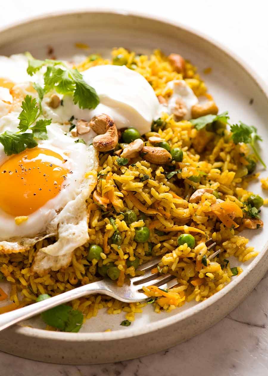 Close up of Curried Rice (basmati rice) with crispy fried egg and a dollop of yogurt on a rustic plate, ready to be eaten