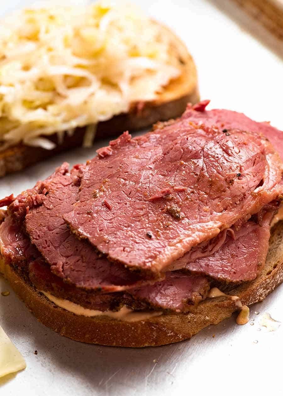 Pastrami being piled onto Reuben Sandwich