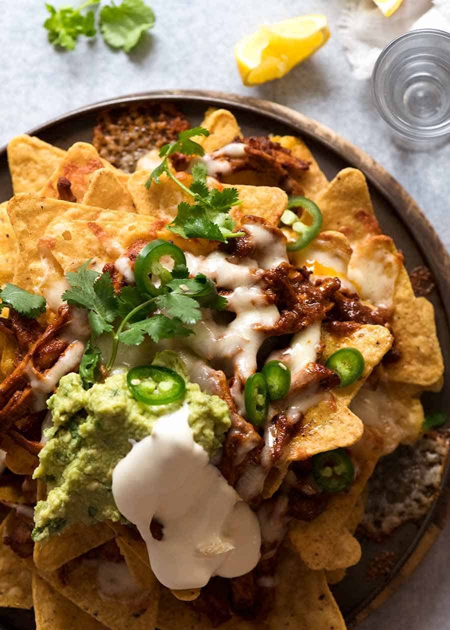 Overhead photo of Chicken Nachos with toppings - sour cream, jalapeño guacamole, coriander / cilantro