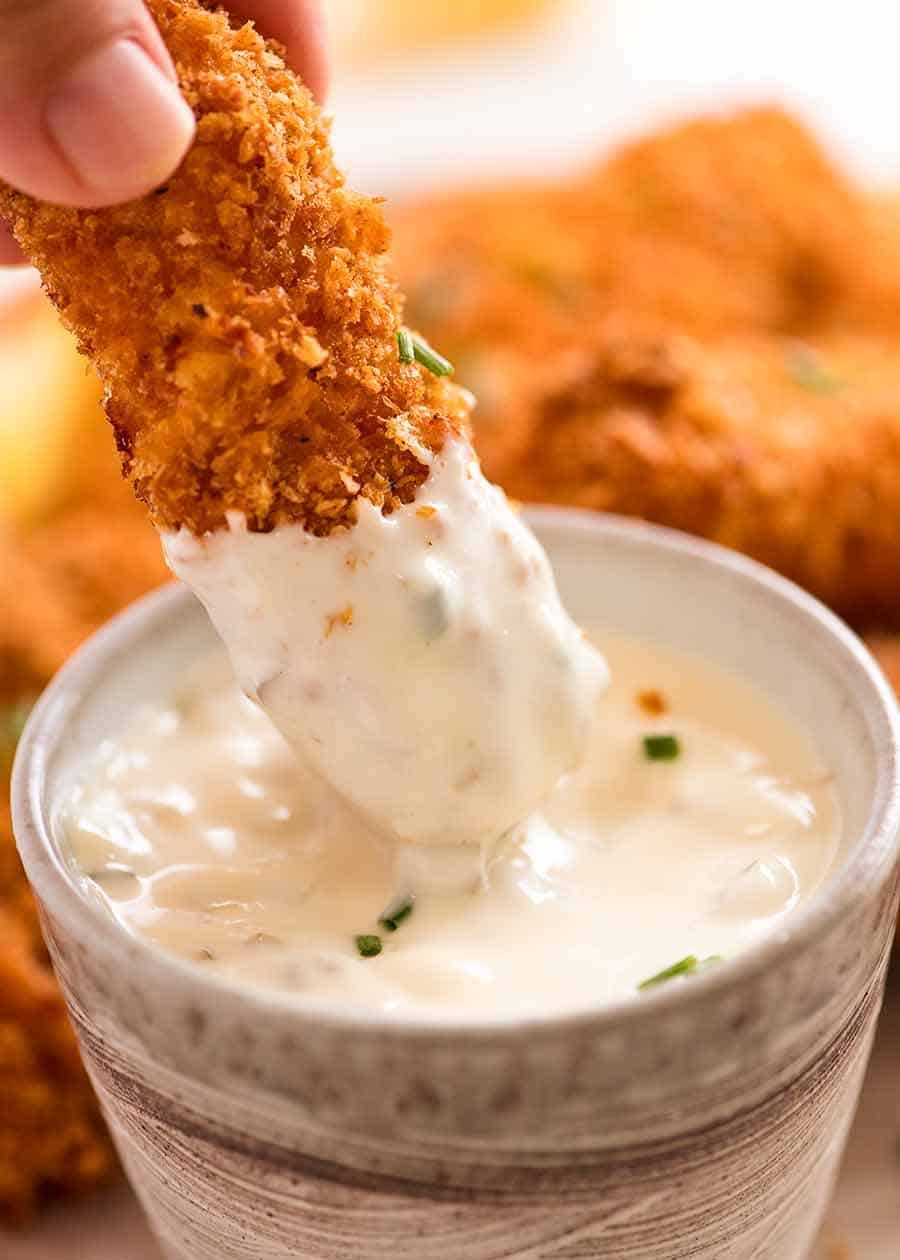 Close up of homemade fish fingers being dipped into tartare sauce