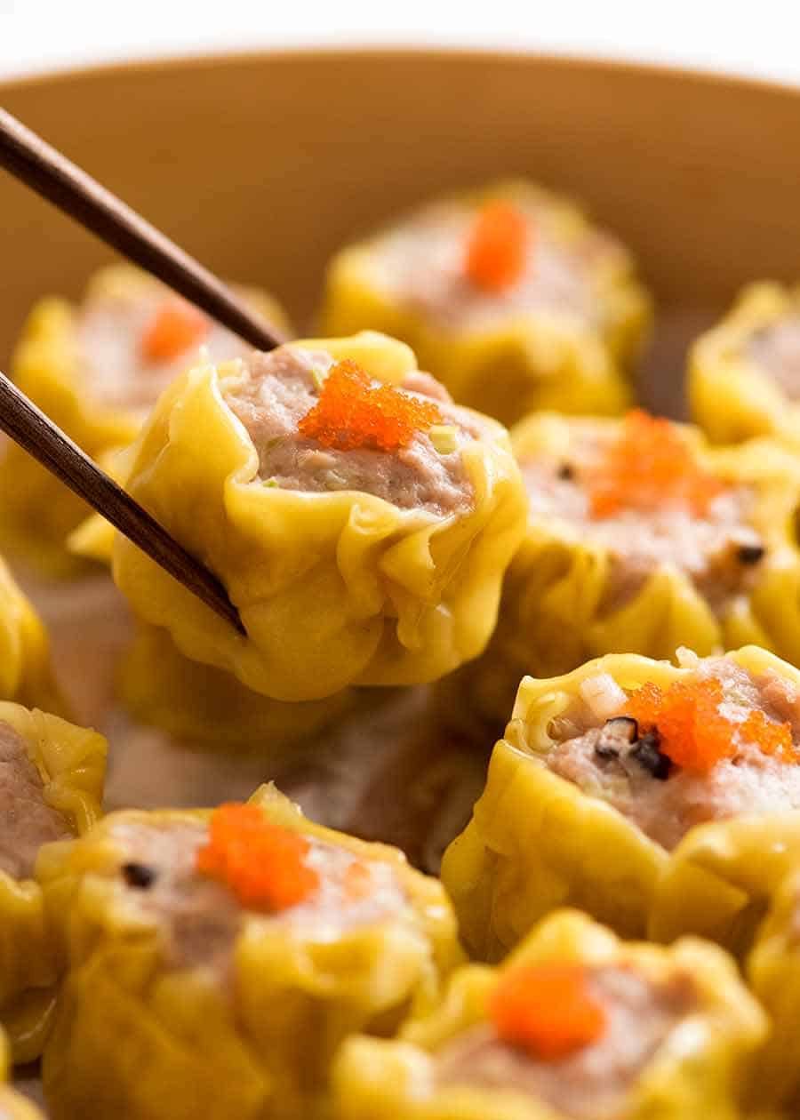 Close up of chopsticks holding Siu Mai (Chinese steamed dumpling) dipped in sauce