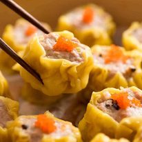 Close up of chopsticks holding Siu Mai (Chinese steamed dumpling) dipped in sauce