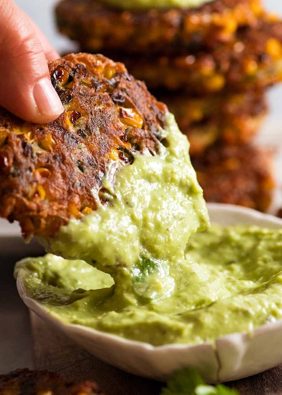 Hand dipping Crispy Corn Fritters into avocado sauce