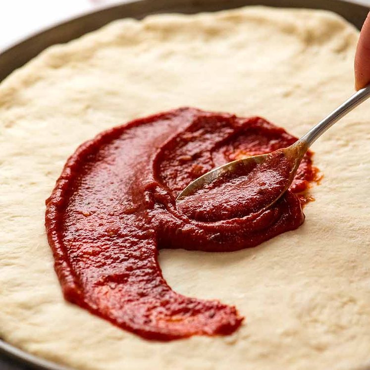 Spreading pizza sauce on homemade pizza crust