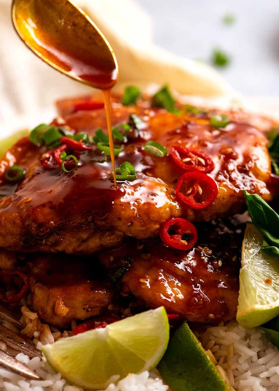 Close up of spoon drizzling sticky spicy sweet sauce over Asian Chilli Chicken