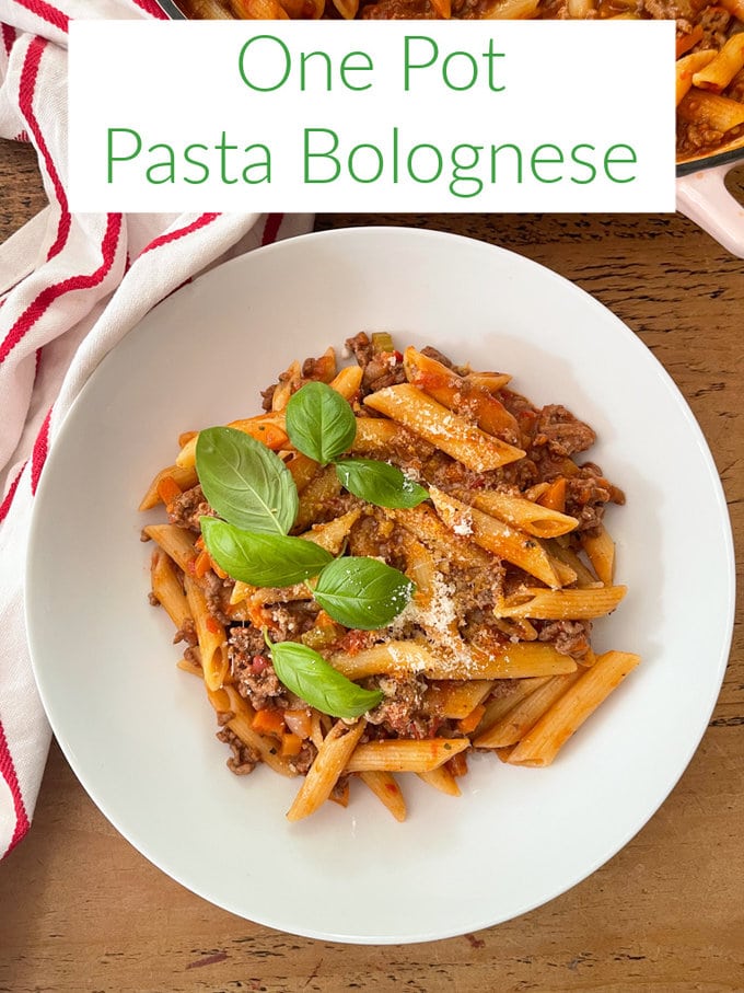 One pot pasta bolognese served in a large,round white pasta bowl, and garnished with grated cheese and basil leaves. 