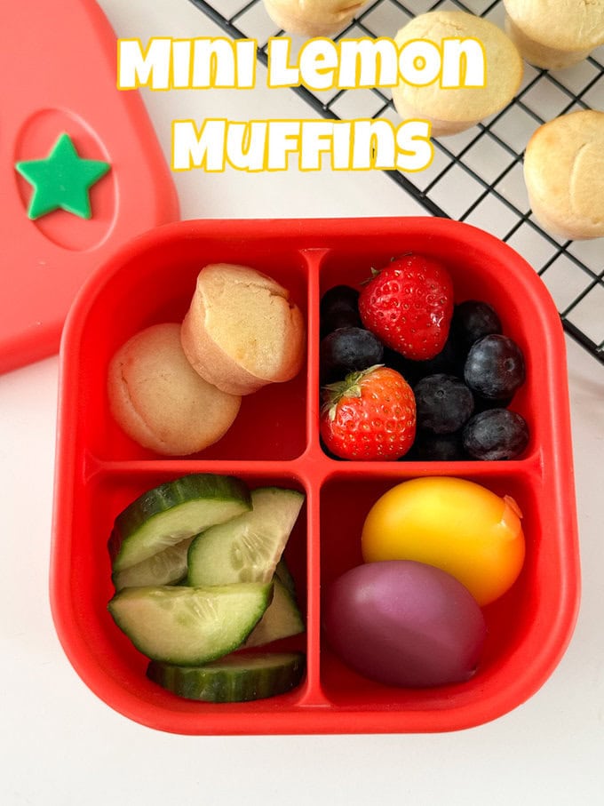 Mini lemon muffins served in a bright red snack box. Along with fresh berries and cheese.