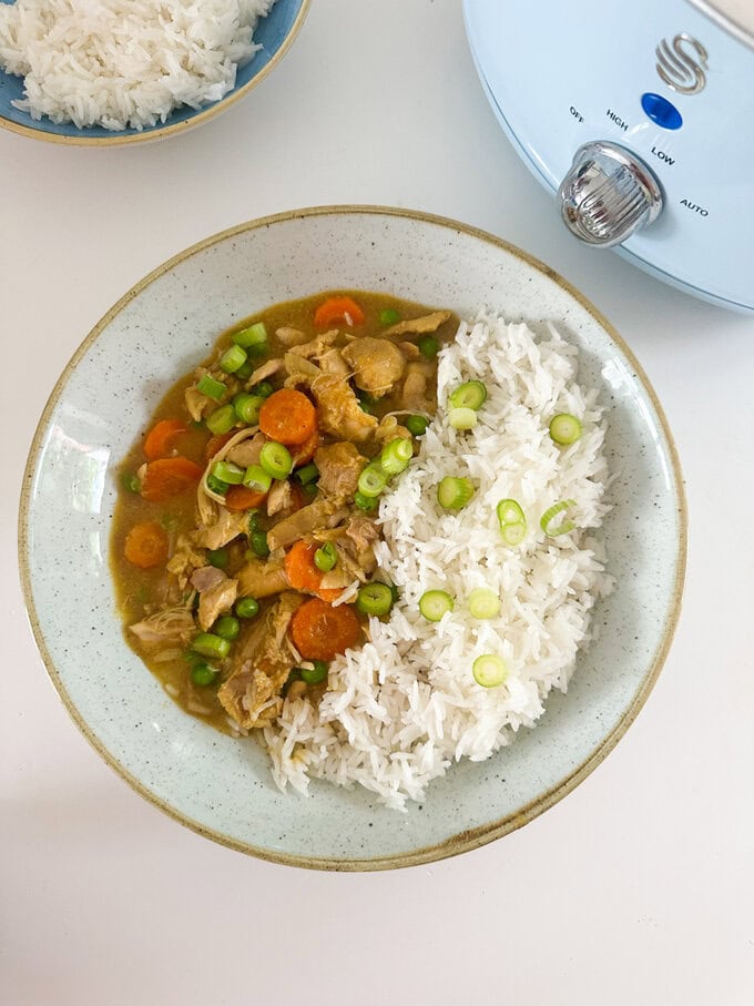 A serving of Slow Cooker Mayflower Chicken Curry served in a bowl with white rice and freshly chopped spring onion.